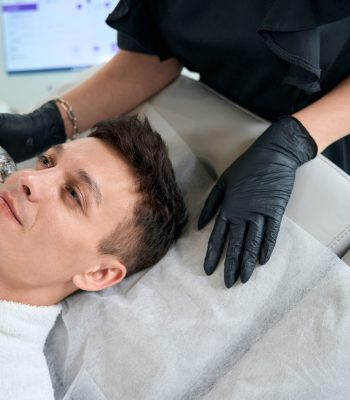 Beautician in protective gloves standing near male and doing microneedle rf-lifting in beauty salon