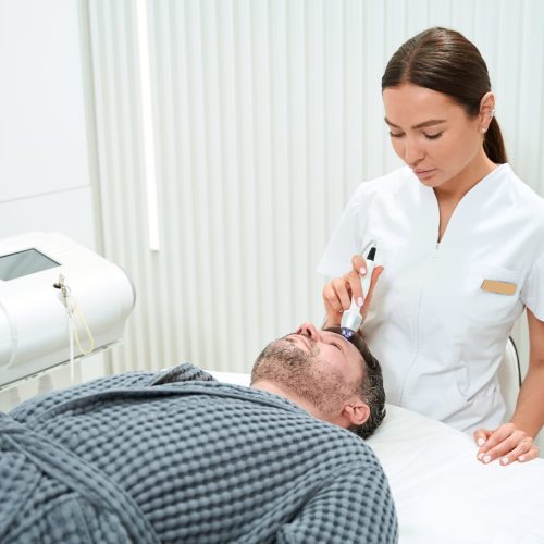 Young cosmetologist performs a non-surgical lifting procedure to a middle-aged man, a specialist uses a modern apparatus